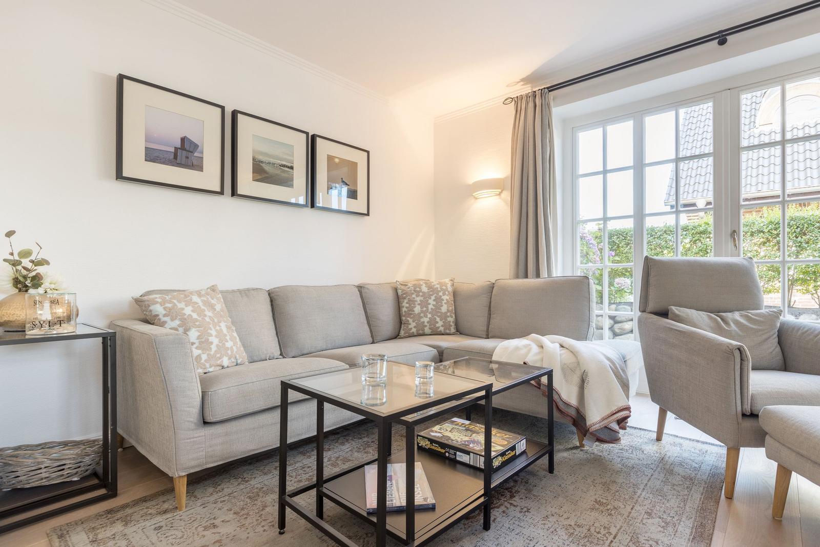 Wohnzimmer mit Sofa, Sessel und Glas-Tisch. Fenster mit Blick auf Garten.