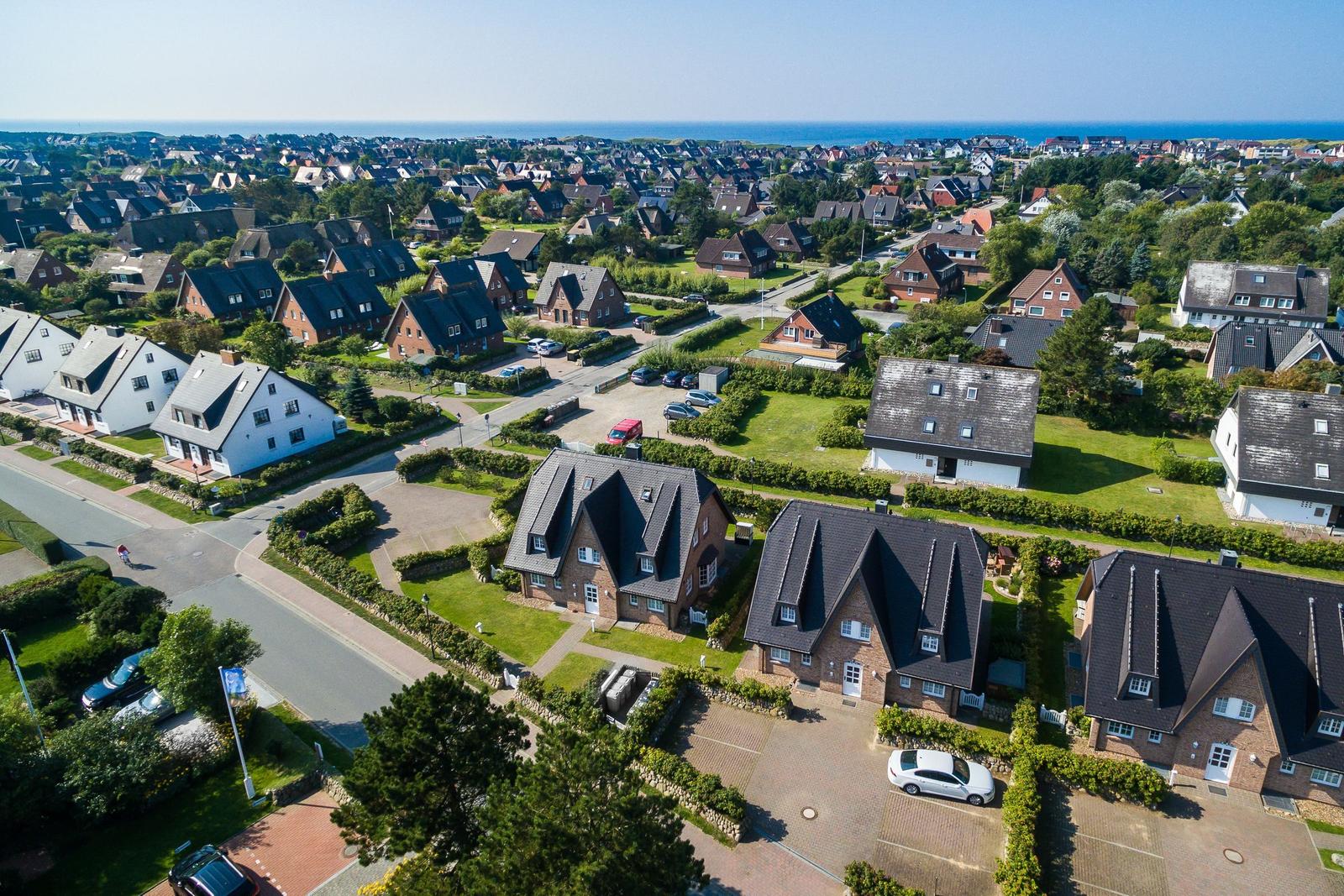 Luftbild von Häusern mit Gärten und Straßennetz in einer Küstenstadt.