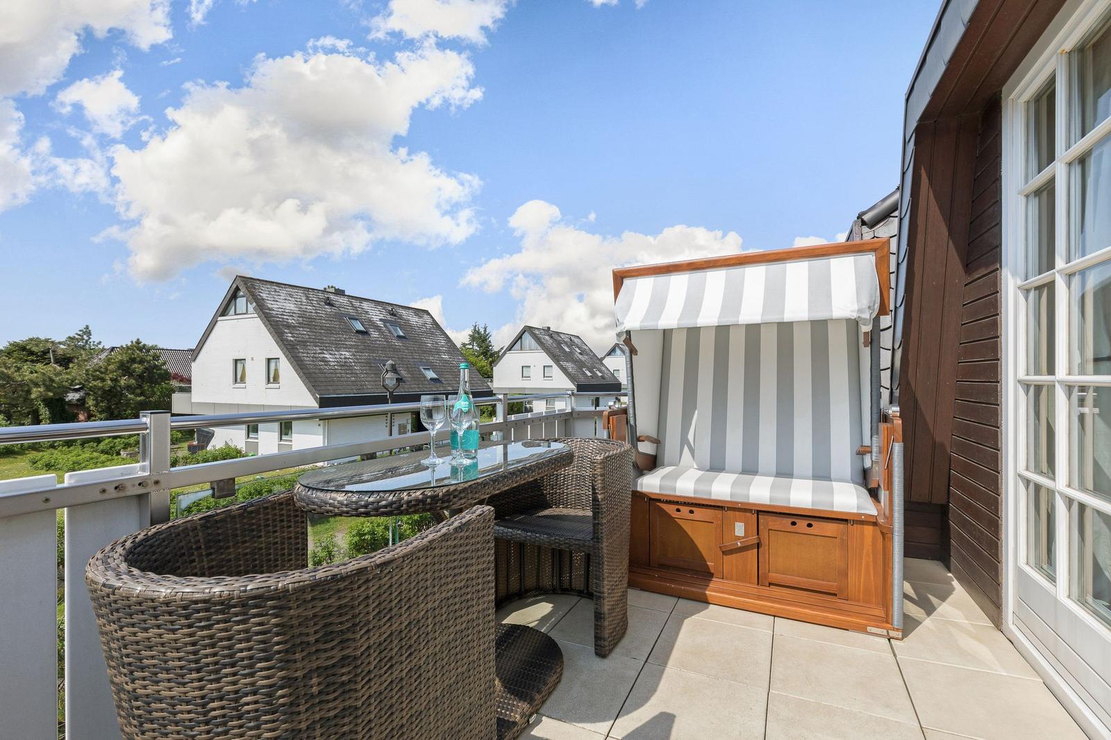 Terrasse mit Liege, Tisch und Stühlen. Blick auf Dächer und Himmel.