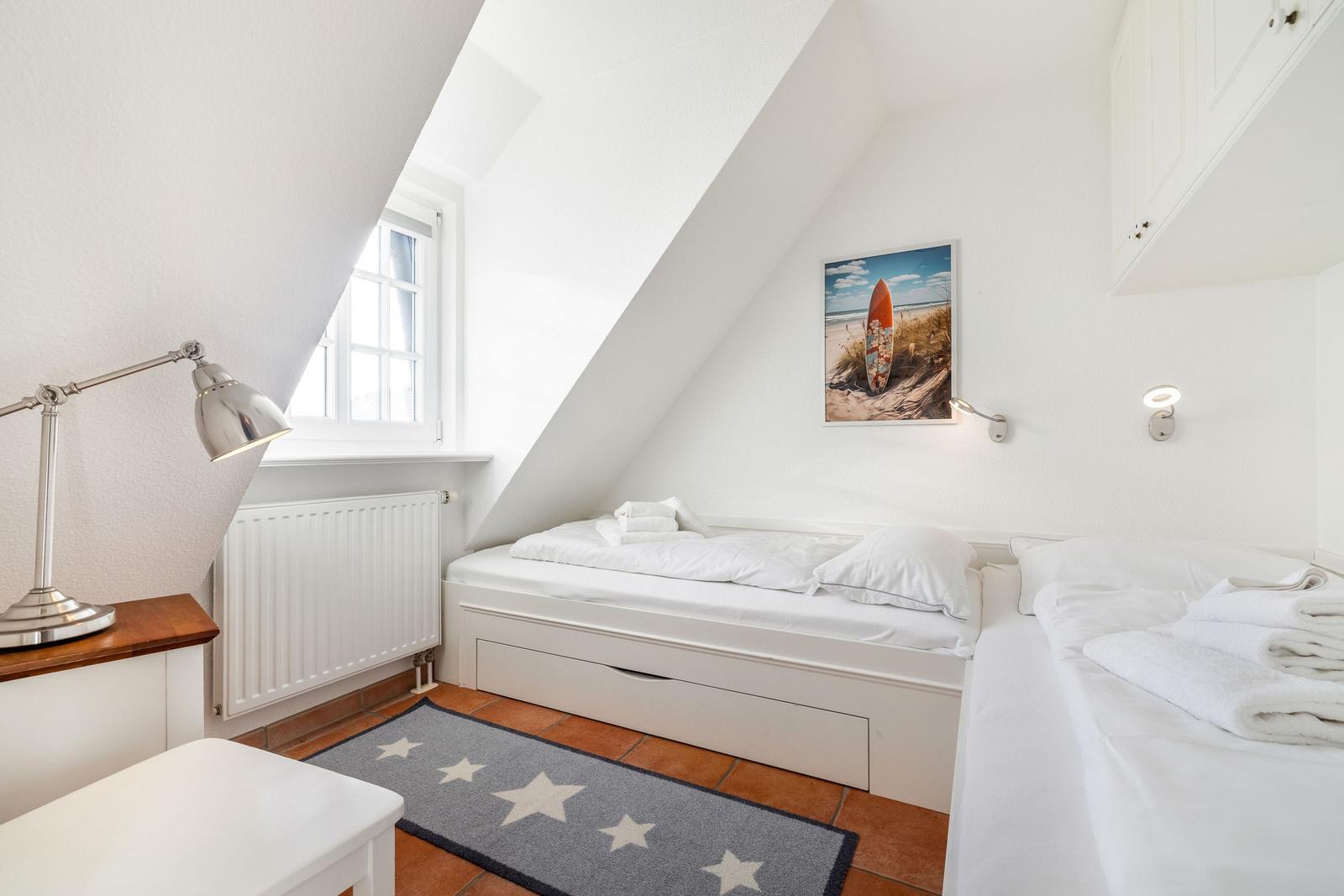 Zimmer mit zwei Betten, Fenster, Heizkörper und Wandbild.