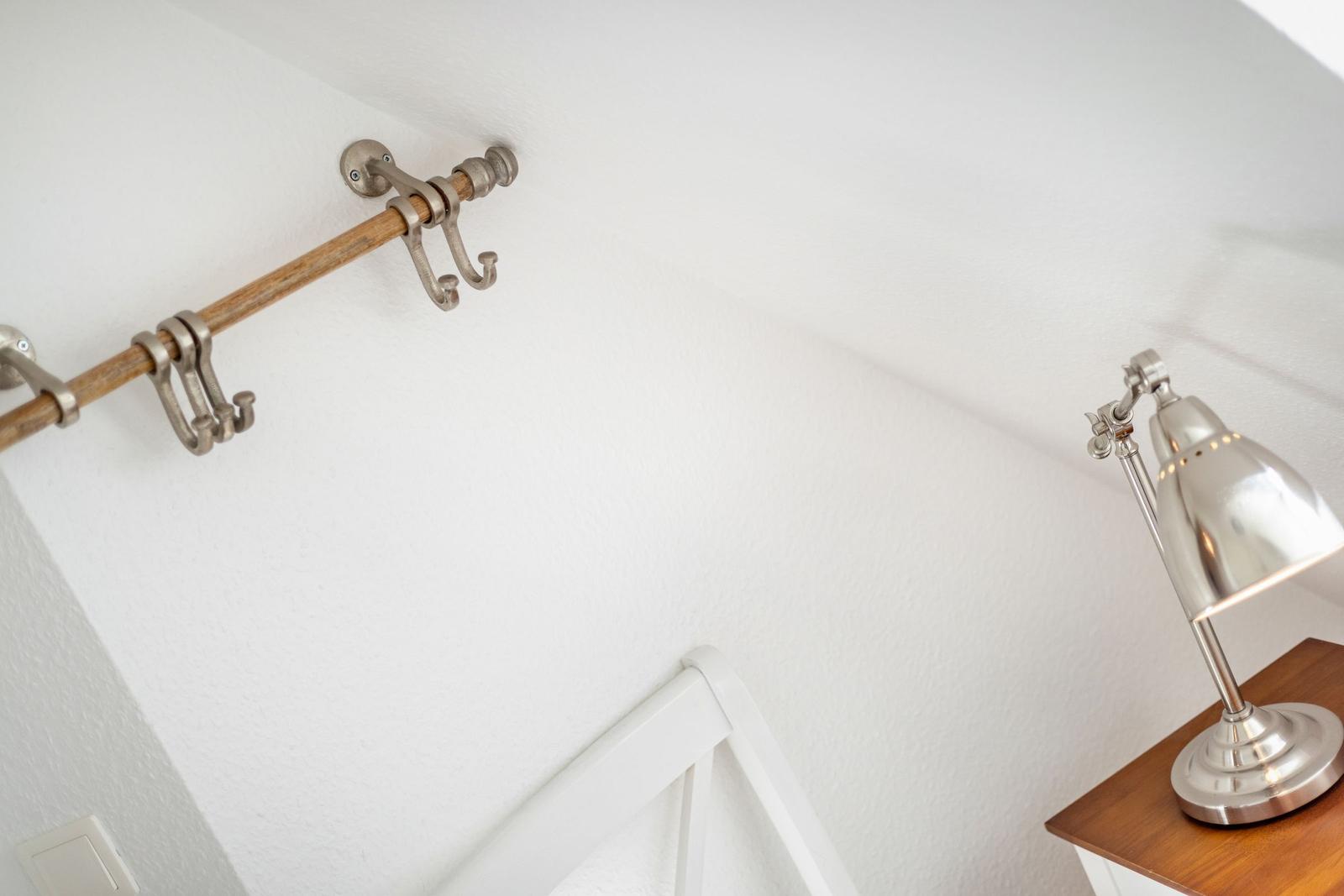 Wandhalterung mit Haken und Schreibtischlampe neben einem Bett.