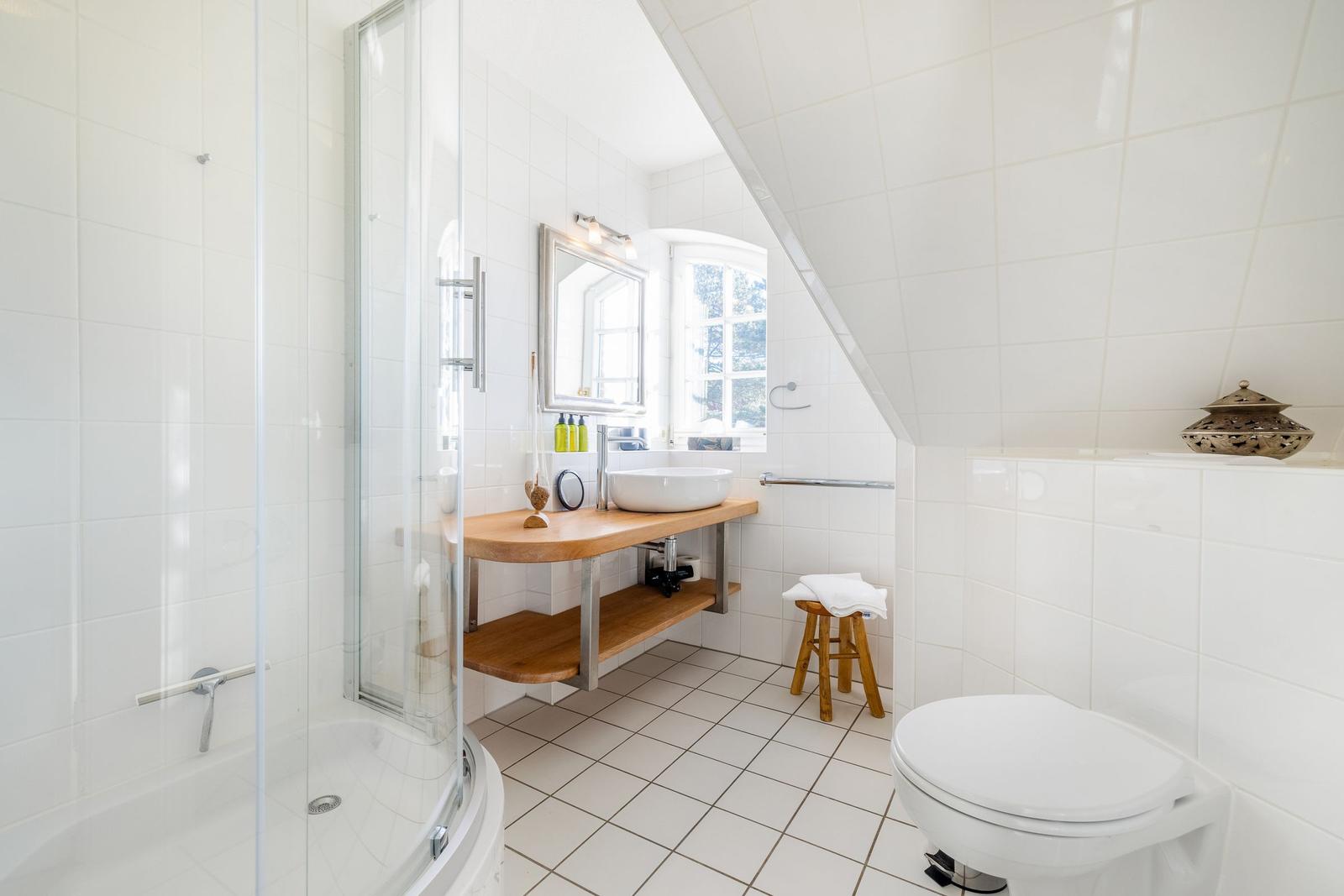 Badezimmer mit Dusche, Waschbecken und Toilette unter schrägem Dach