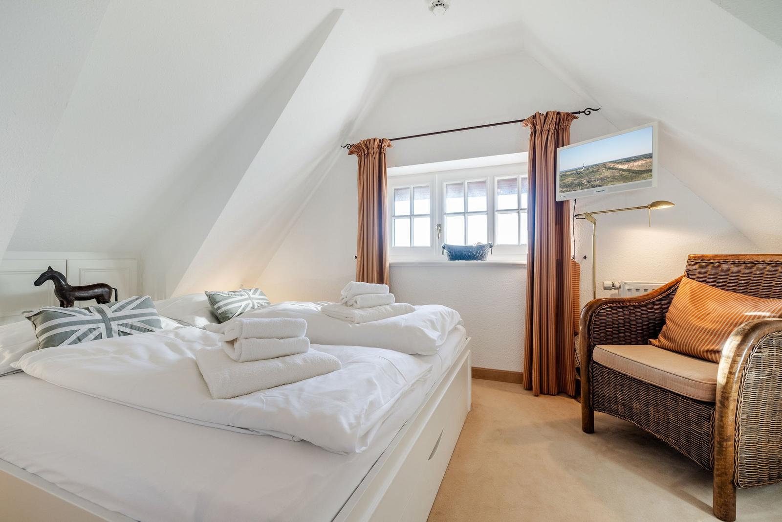 Schlafzimmer mit Dachschrägen, Bett, Sessel und TV.