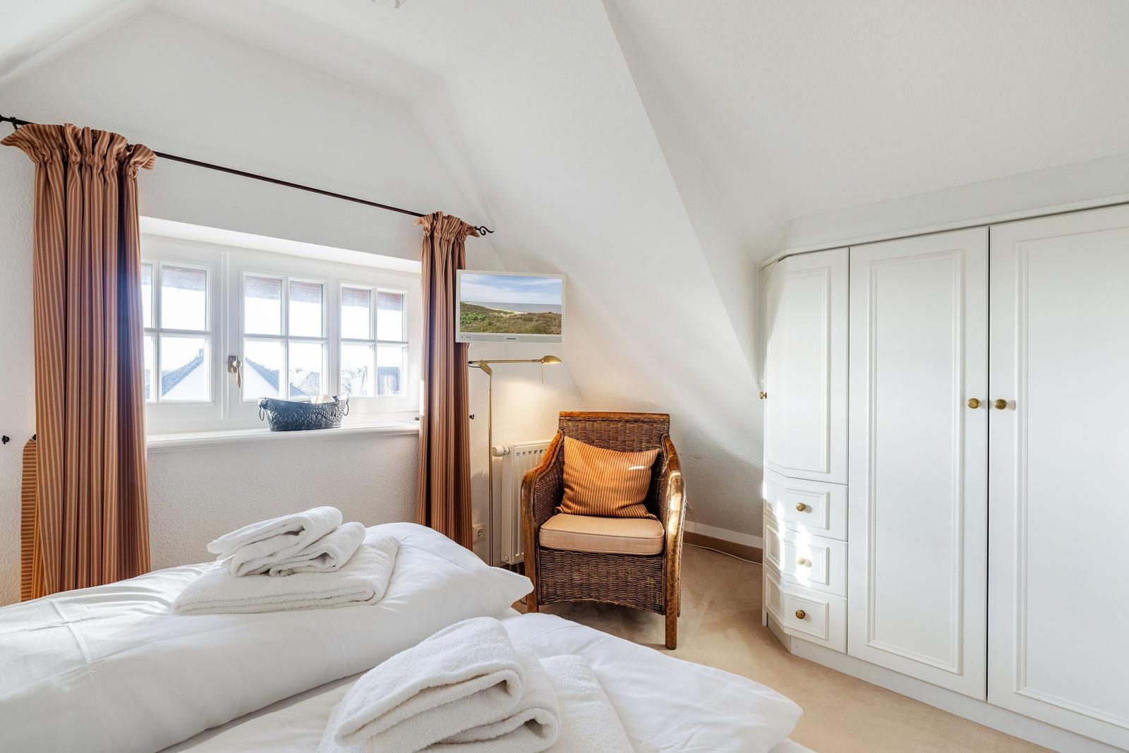 Schlafzimmer mit Dachschrägen, Bett, Schrank und Sessel.
