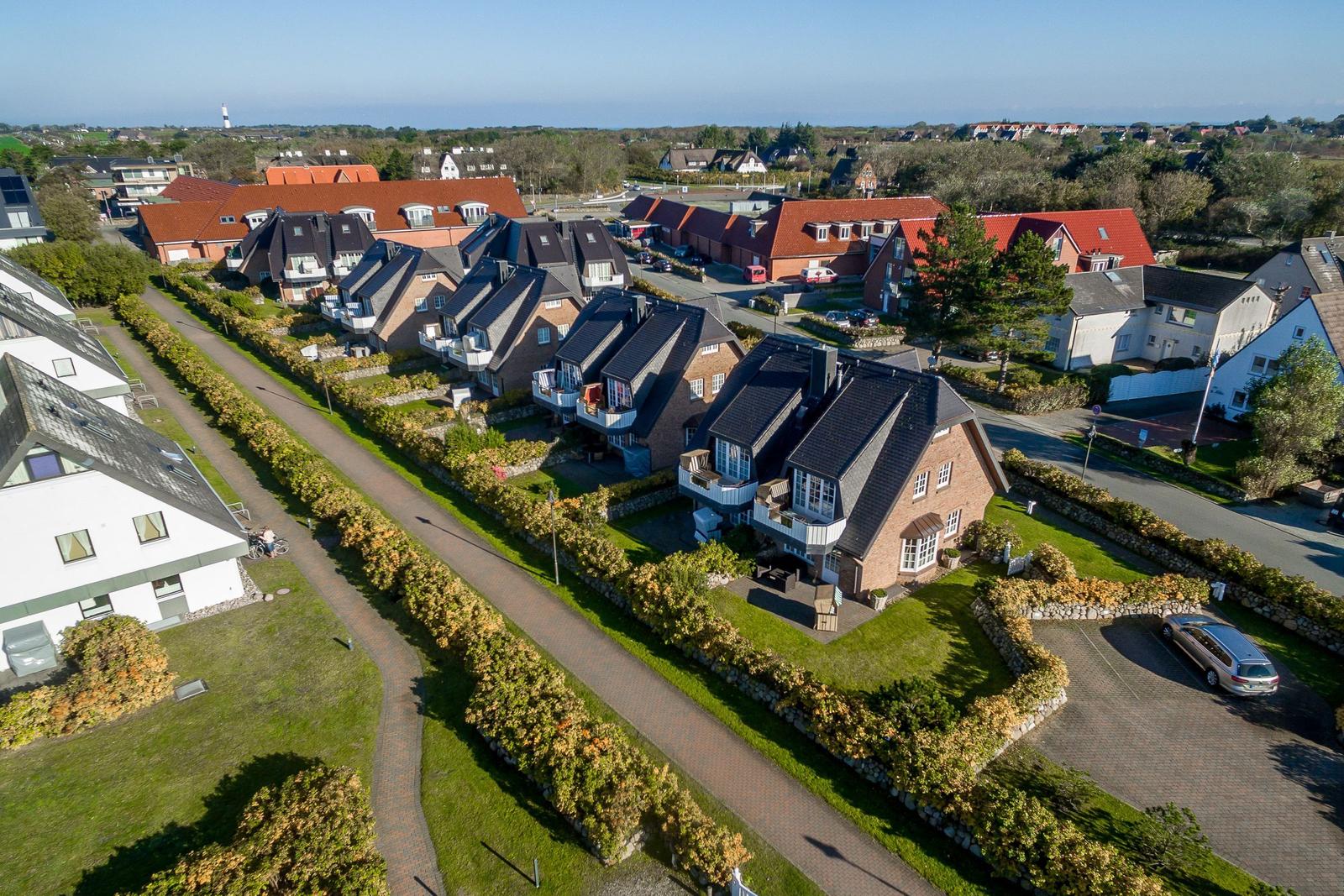 Aerial view of a residential area with houses, gardens, and a paved path.