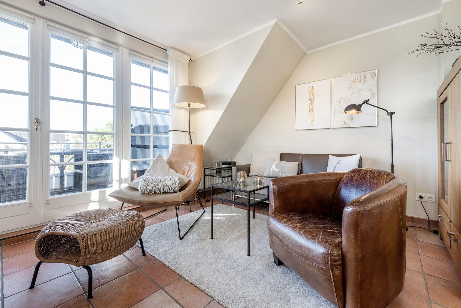 Wohnzimmer mit braunen Ledermöbeln, Glas-Tisch und großen Fenstern.