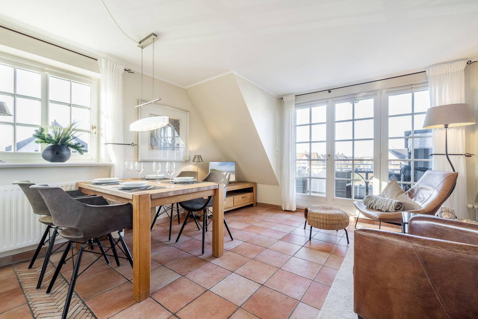 Essbereich mit Tisch, Stühlen und Fenstern. Wohnbereich mit Ledersofa und Sicht auf Balkon.