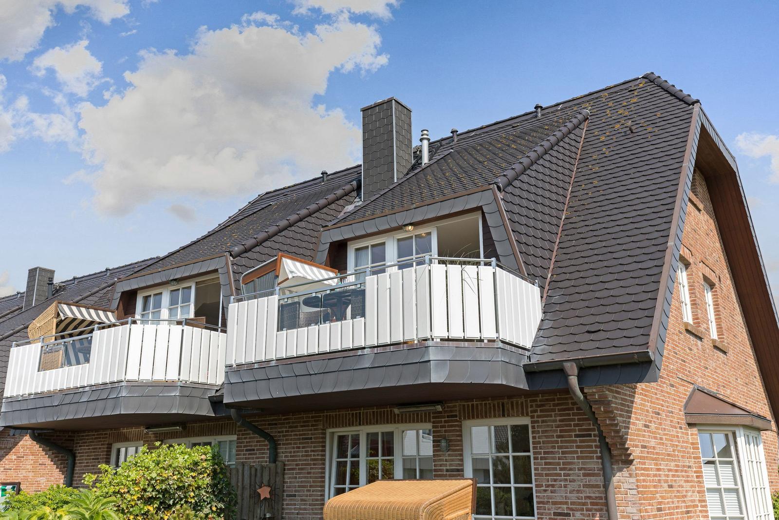 Zweistöckiges Haus mit Balkonen und Ziegelfassade unter blauem Himmel.