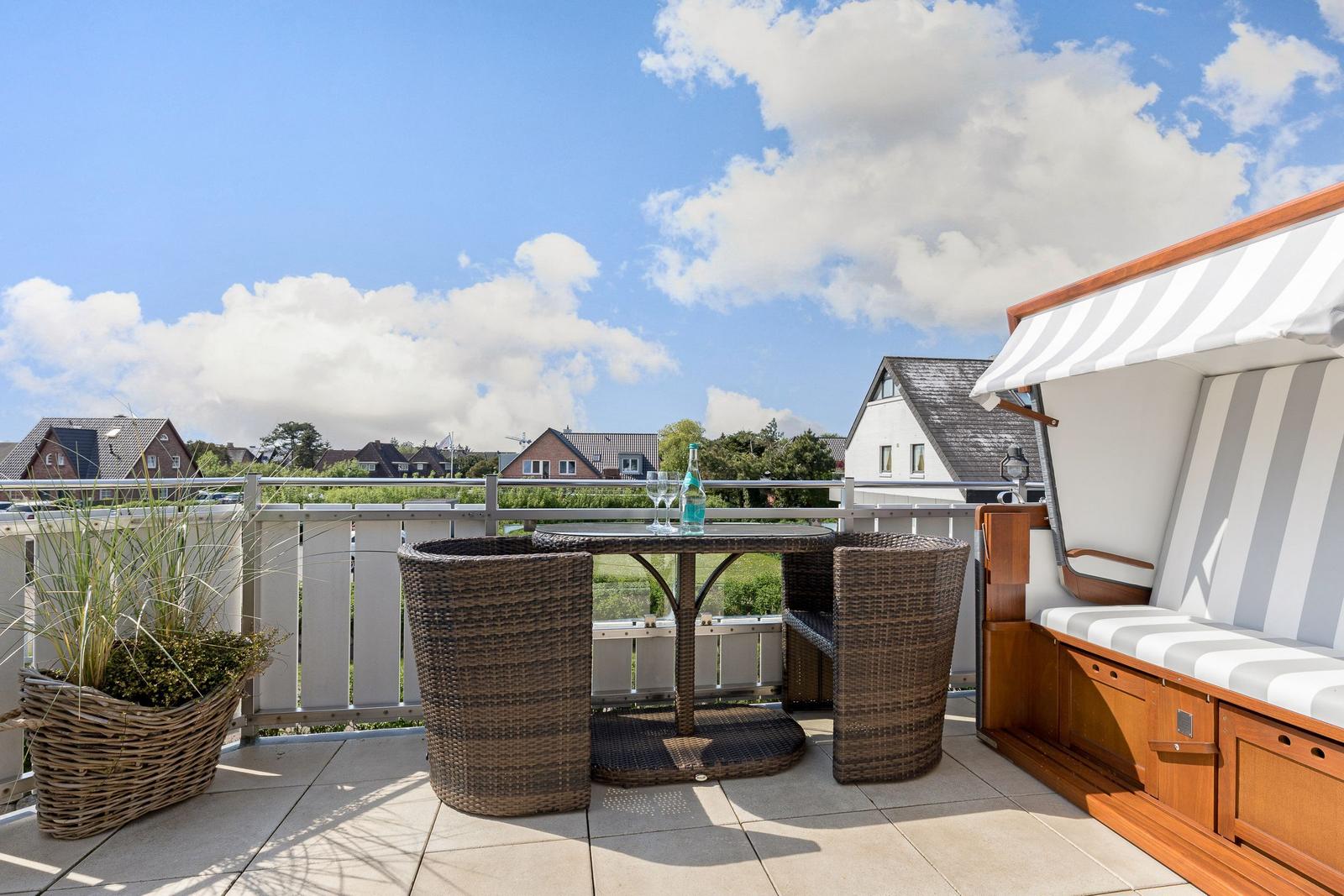 Terrasse mit Tisch, Stühlen und Sonnenschutz. Blick auf Wohnhäuser und Grünflächen.