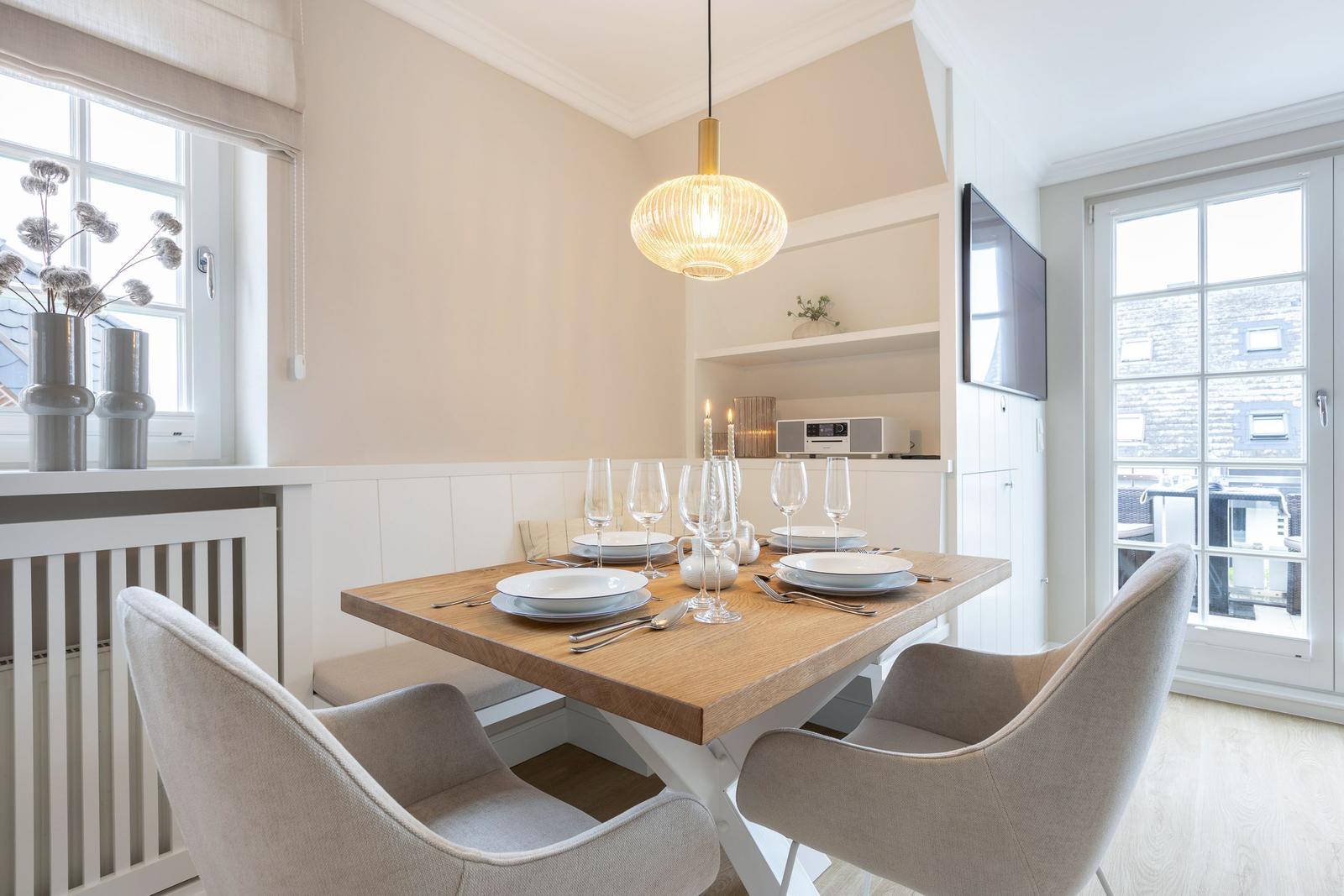 Dining room with wooden table, chairs, and windows. Ceiling light and TV visible.