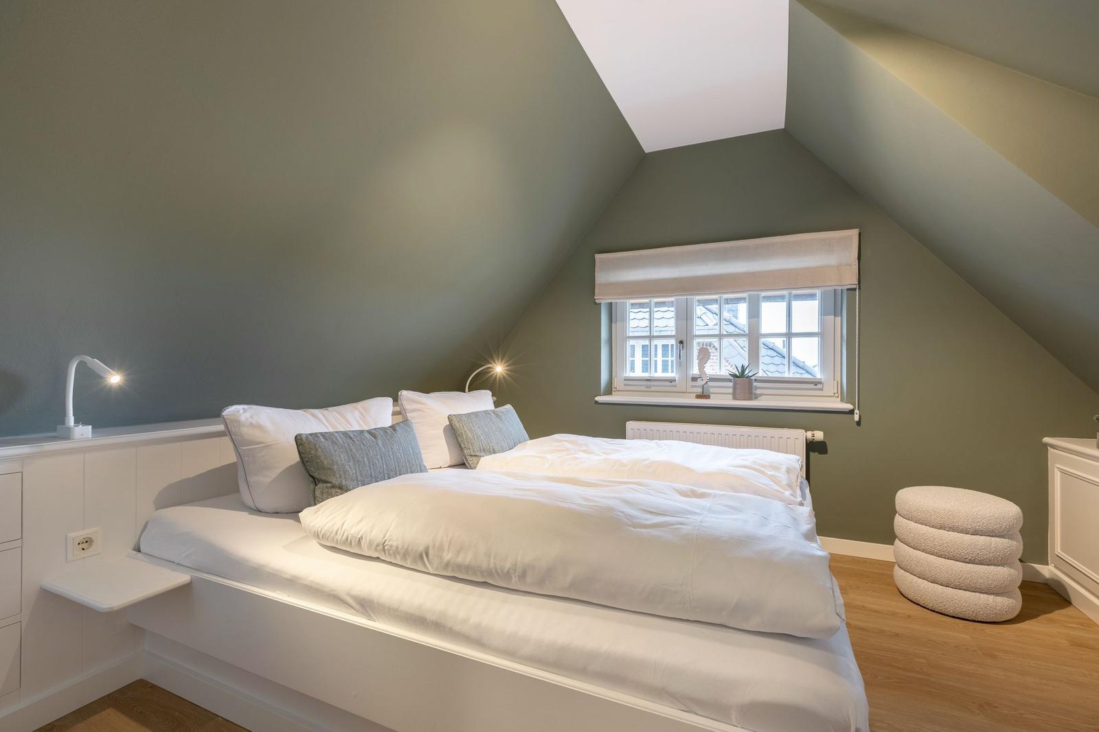 Bedroom with sloped ceiling, bed, window, and stool.