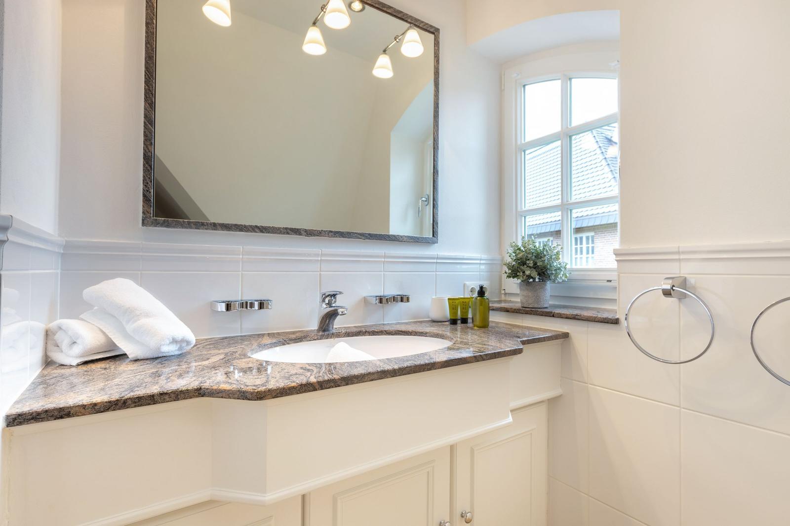 Bathroom with sink, mirror, and window. Towels and care products on the countertop.