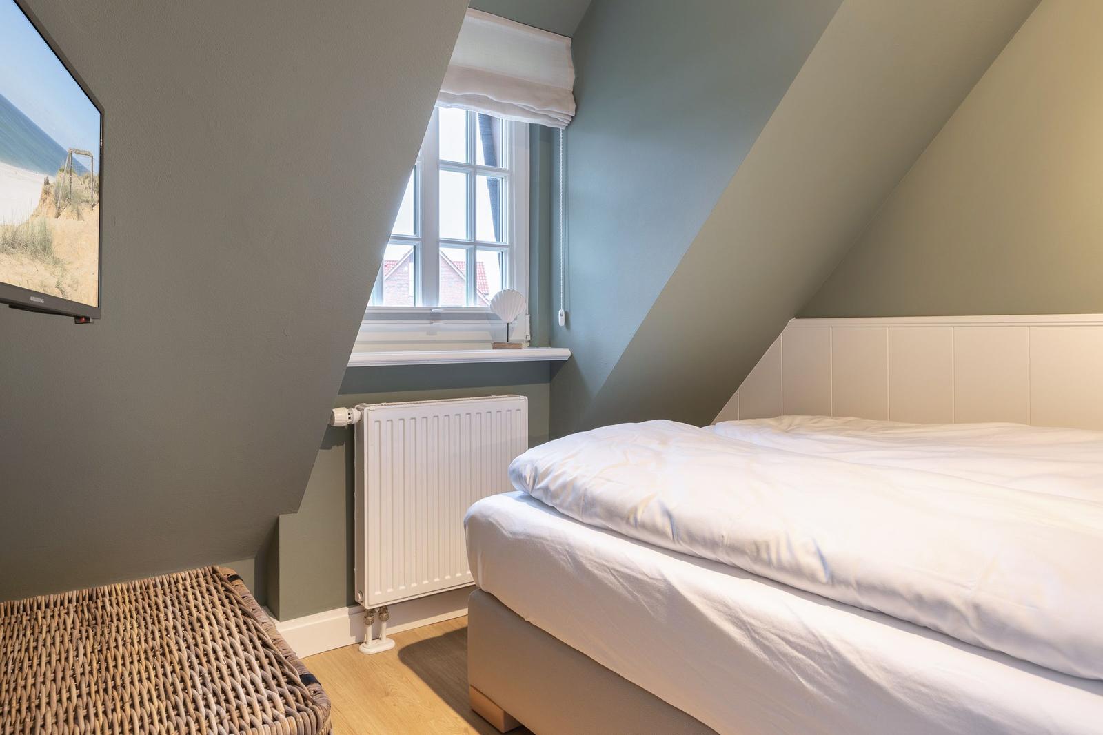 Bedroom with sloped ceilings, window, bed, and radiator.