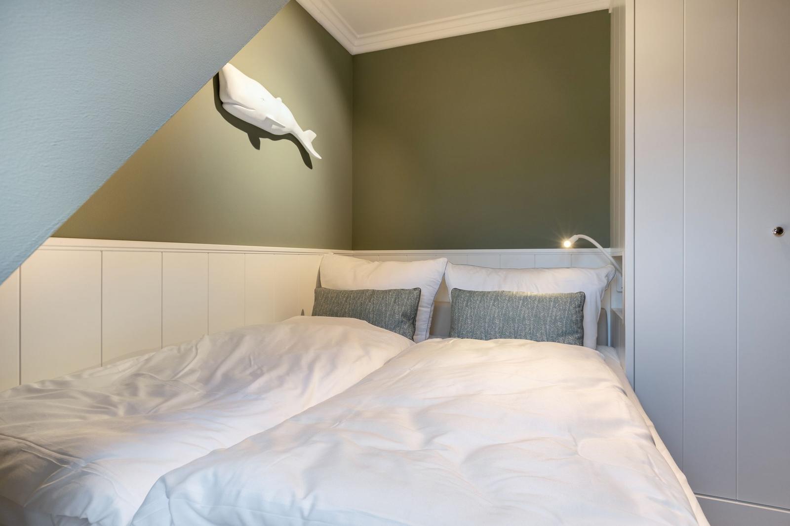 Bedroom with double bed, wall lamp, and whale decoration.