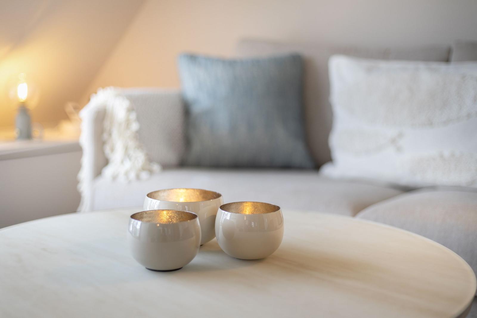 Three gold-rimmed cups sit on a round table in front of a sofa with cushions.