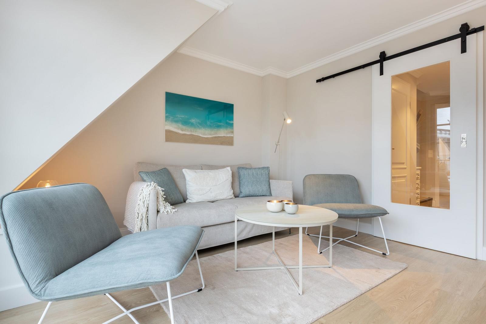 Living room with sofa, two chairs, and round table under sloped ceiling.