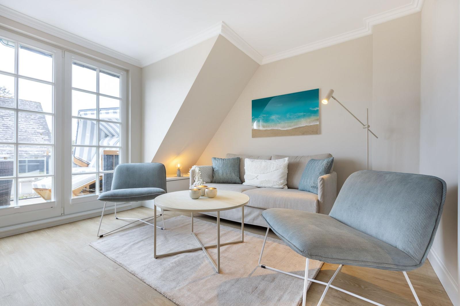 Living room with sofa, two chairs, and table under sloped ceiling with window.