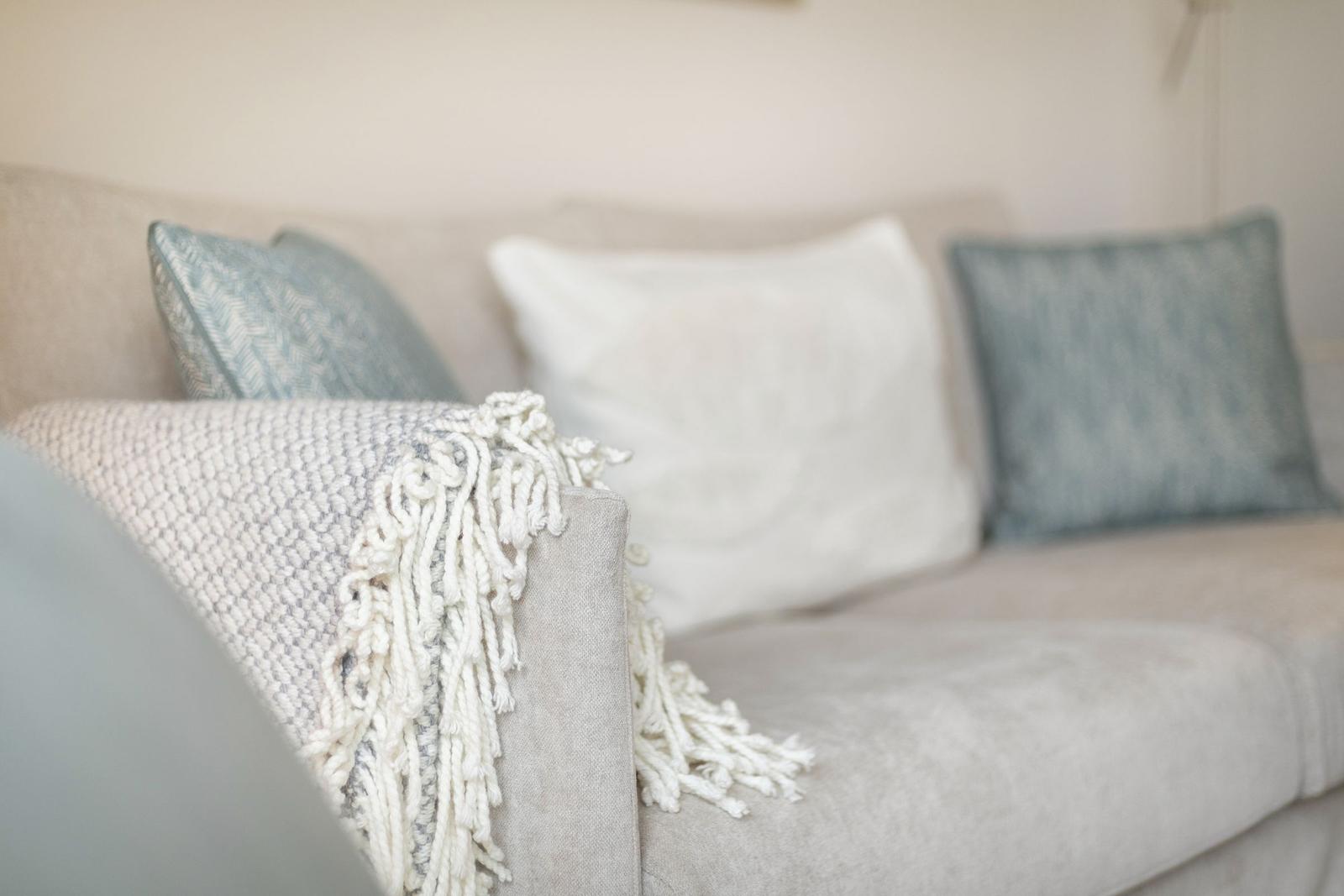 A sofa with cushions and a fringe blanket.