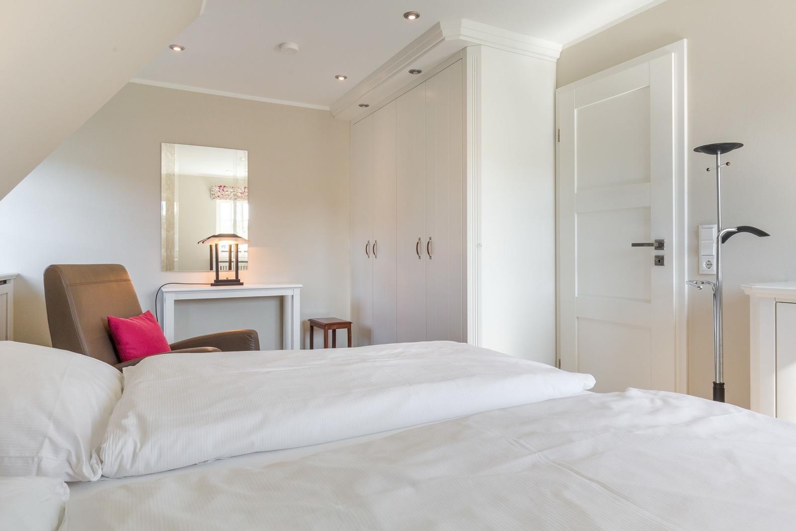 Schlafzimmer mit Bett, Kleiderschrank und Sessel.