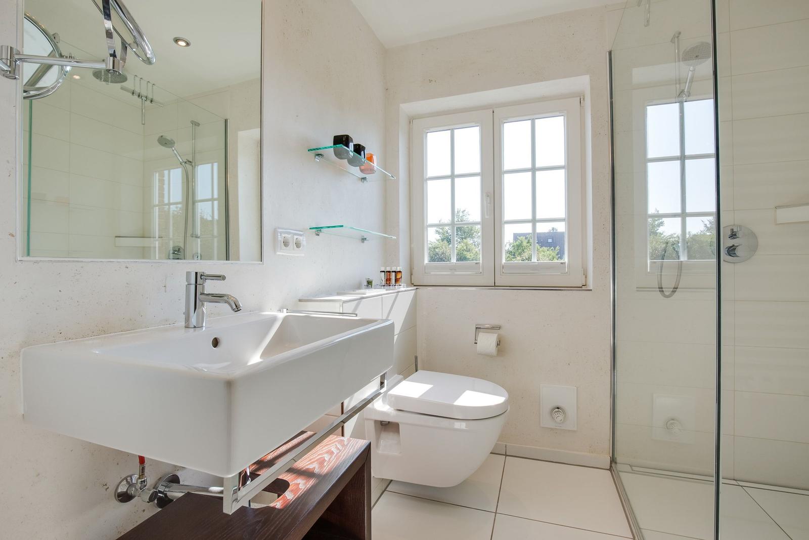 Badezimmer mit Dusche, Waschbecken und Toilette. Fenster mit Blick auf Grün.