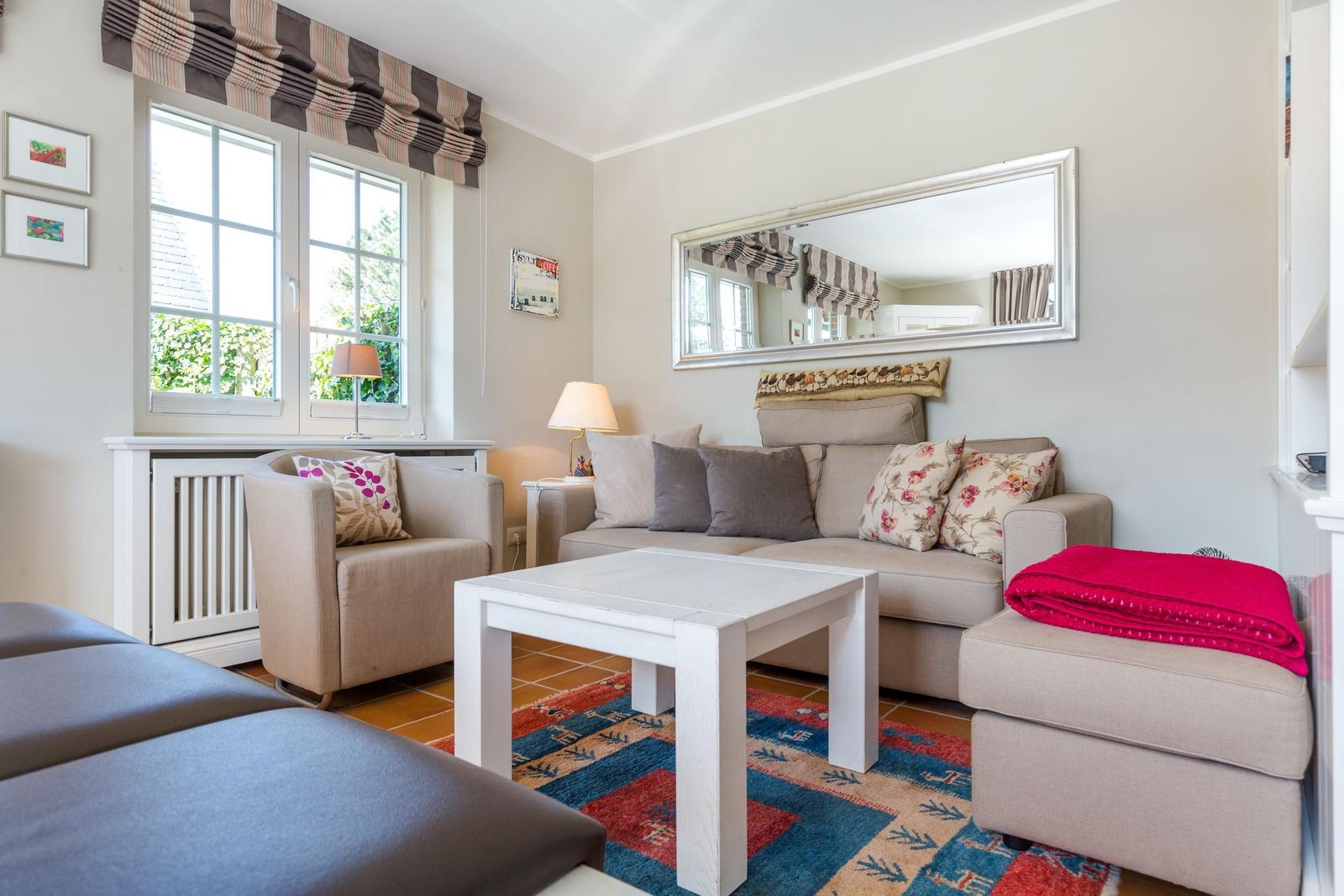 Wohnzimmer mit Sofa, Sessel und Tisch. Fenster, Spiegel und Teppich sind sichtbar.