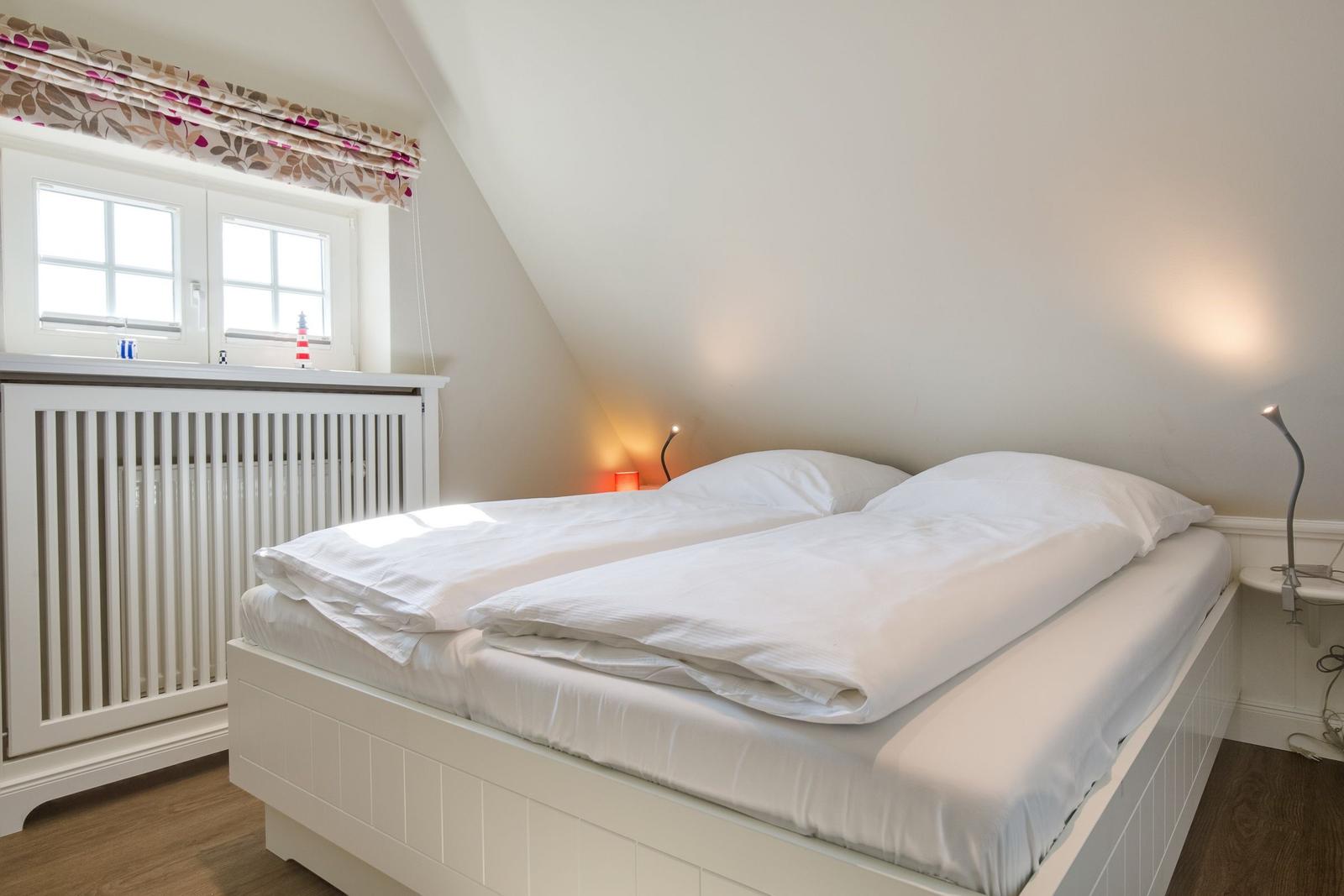 Schlafzimmer mit Doppelbett, Fenster und Stehlampe.