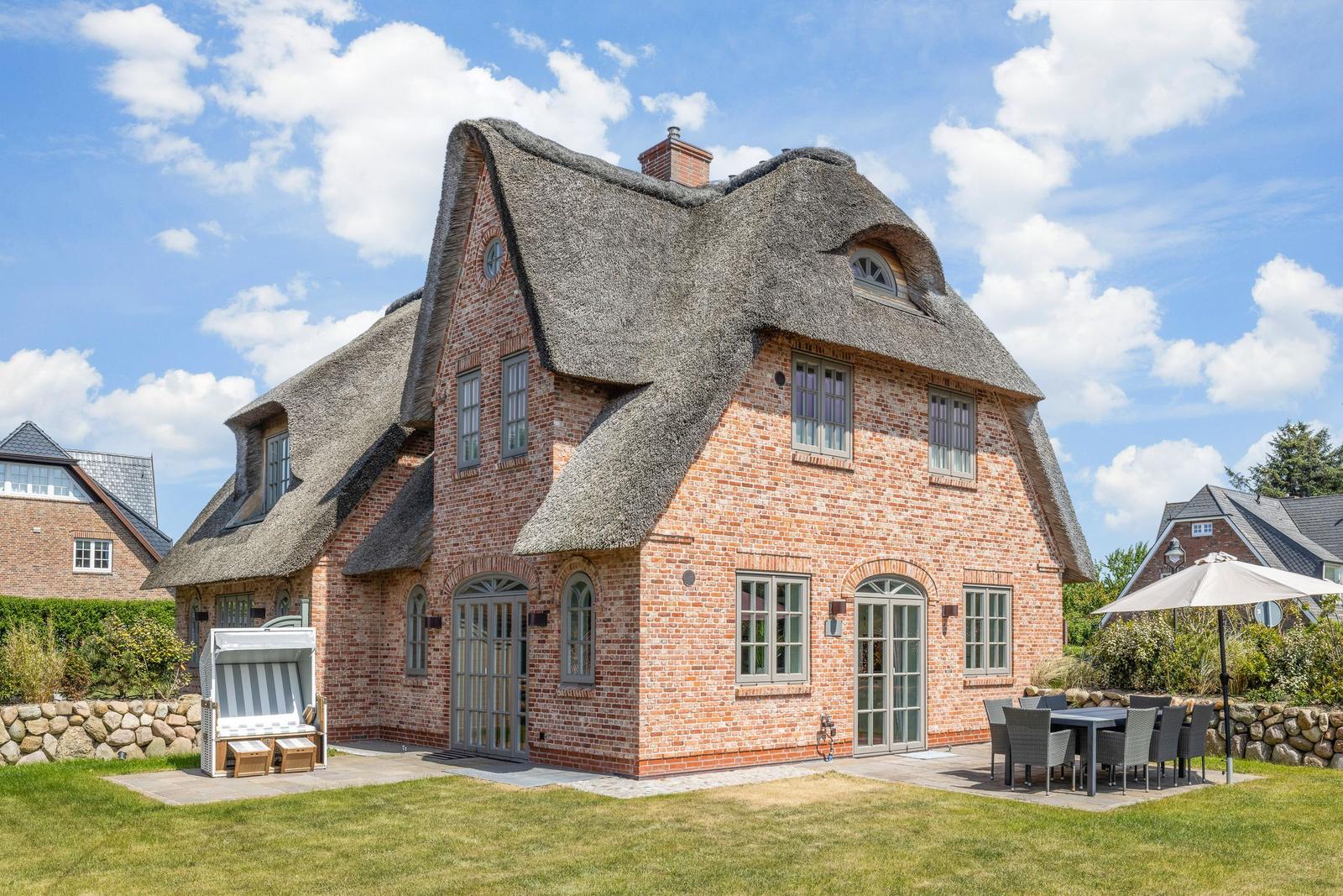 Red brick house with thatched roof and garden area with table and umbrella.
