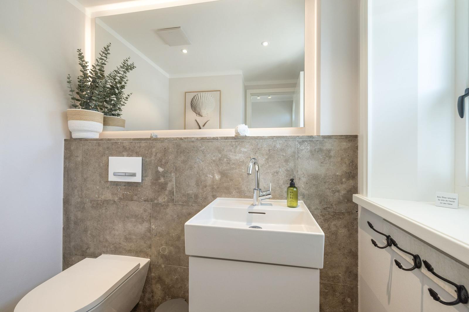 Bathroom with sink, mirror, and toilet. Wall with stone tiles.