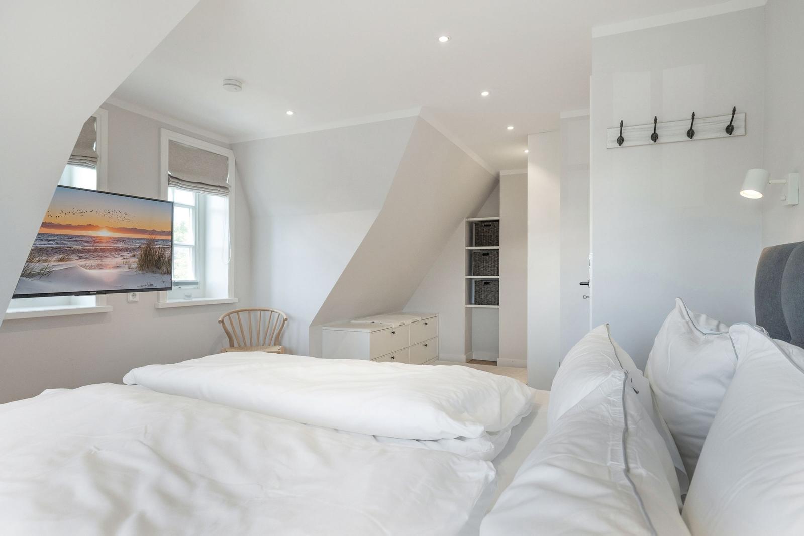 Bedroom with sloped ceiling, bed, TV, and coat rack.