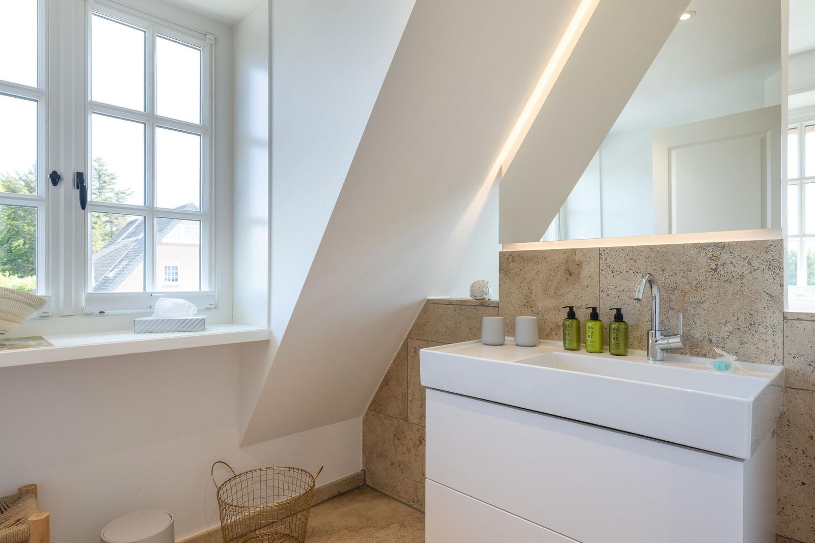 Bathroom with sink, mirror and window. Sloped ceiling and stone wall.