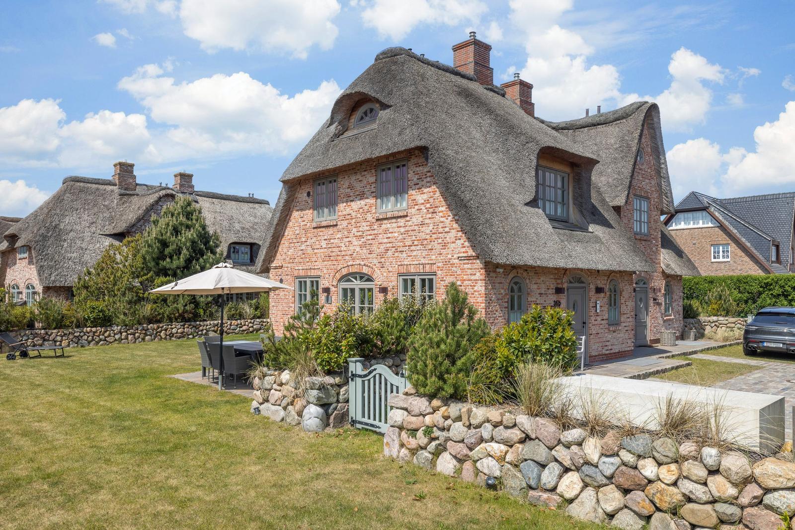 House with thatched roof and stone wall in the garden.