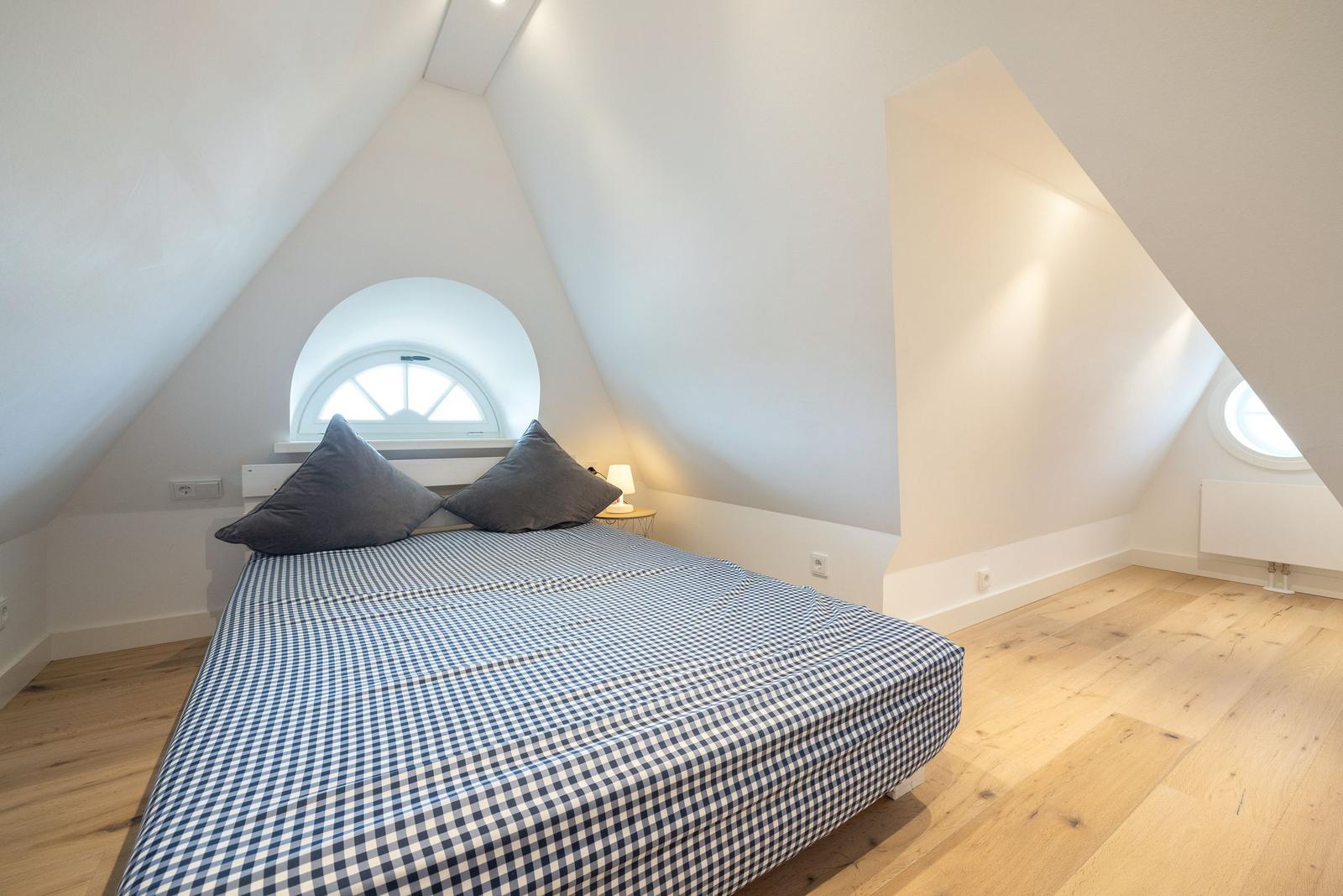 Bedroom with sloped ceiling, wooden floor, and round window.