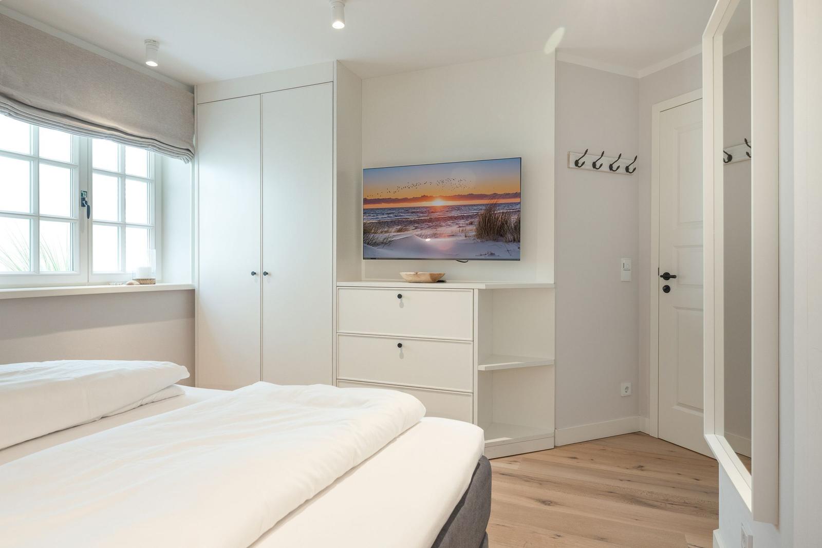 Bedroom with white bed, wardrobe, and TV mounted on the wall.