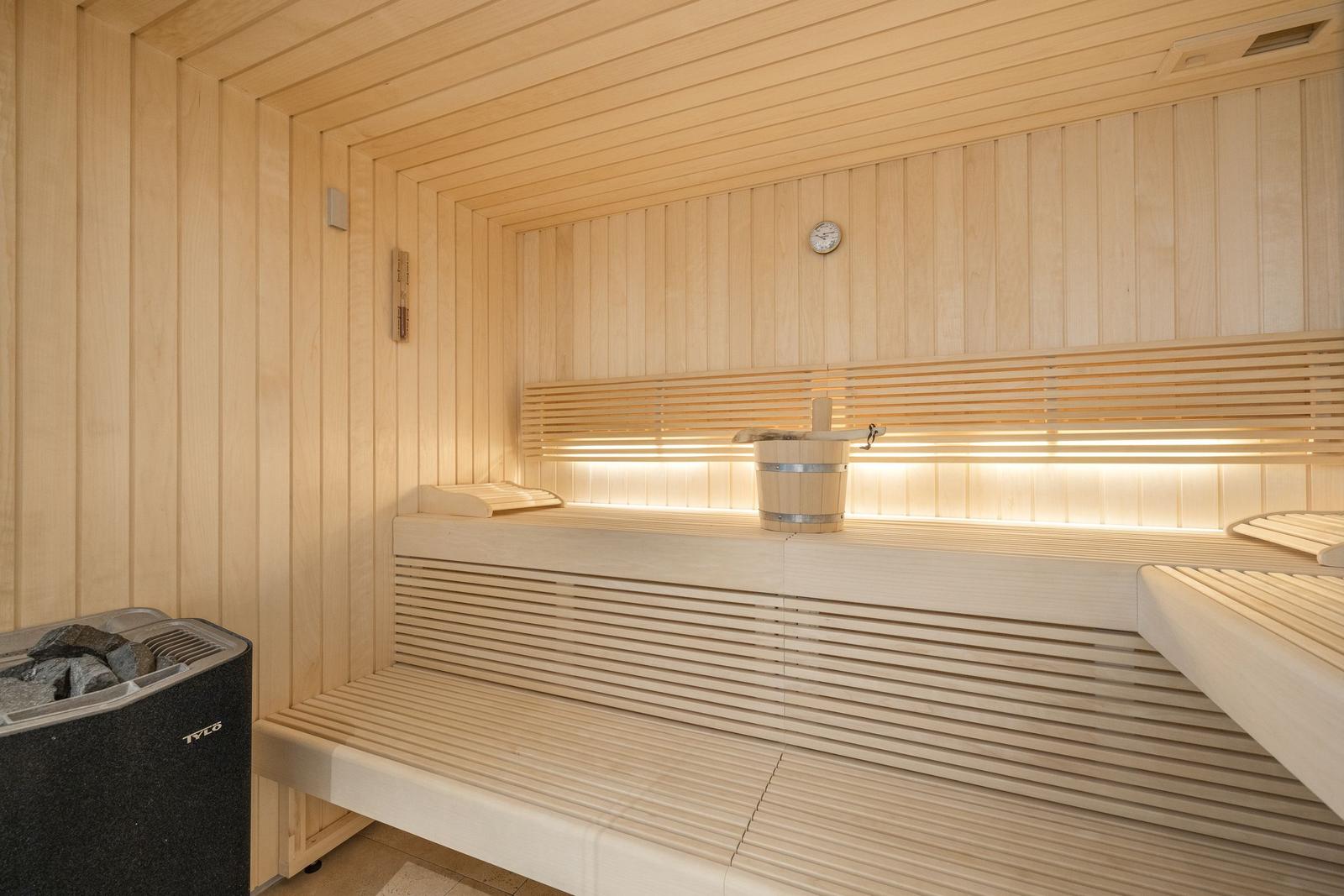 Sauna with wooden benches, thermometer, and wooden bucket