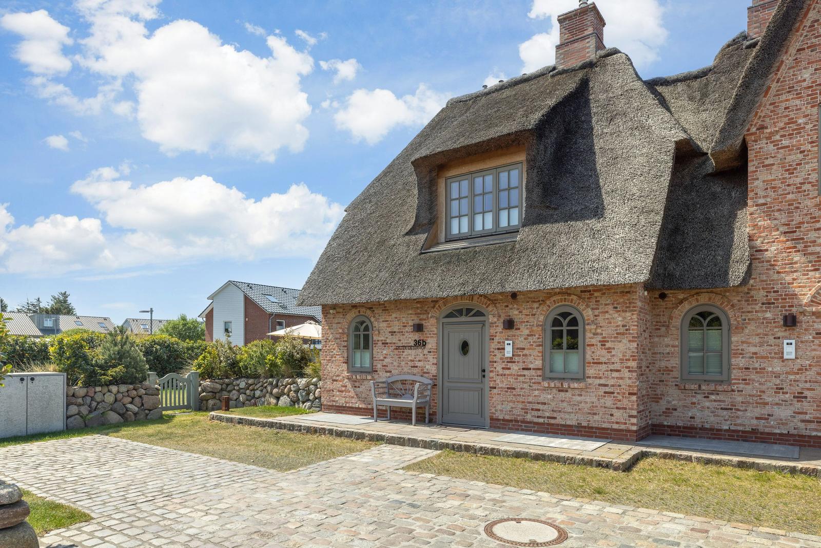 House with thatched roof and brick facade. Gray door and windows.