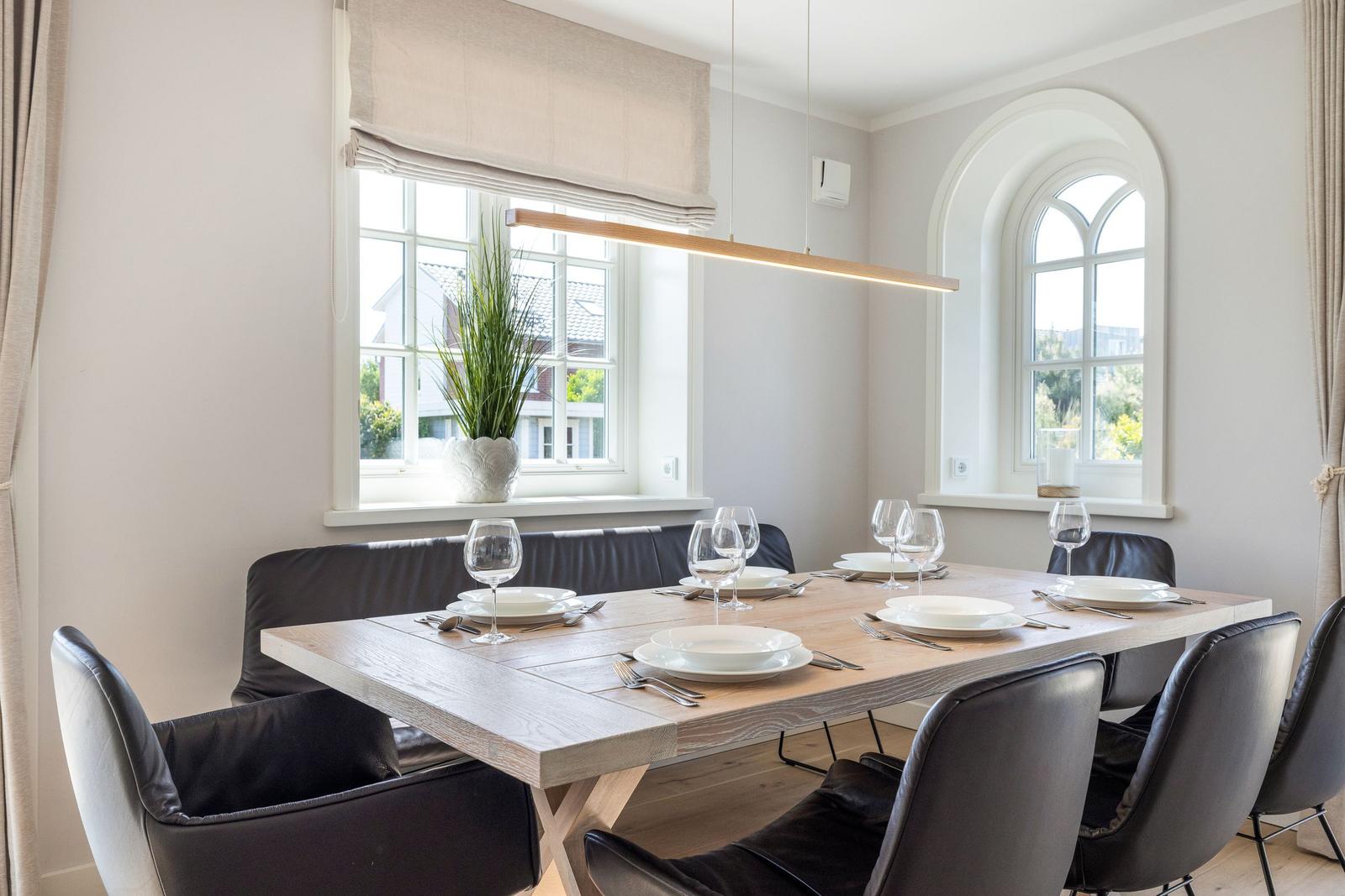Dining room with wooden table, black chairs, and two windows overlooking outside.