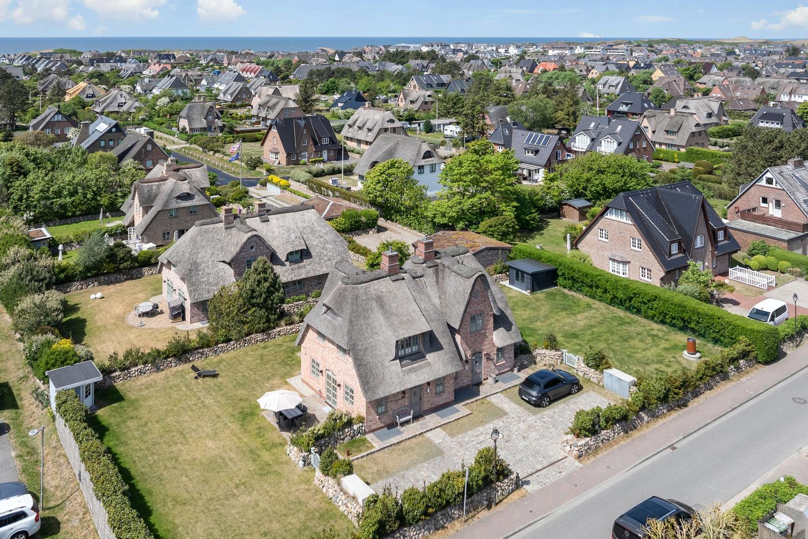 Thatched-roof house with garden. View of coastal town with sea in background.
