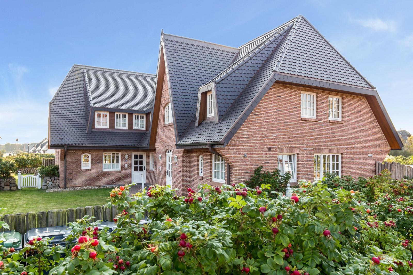 Red brick house with dark gabled roof and rose bushes in the foreground.