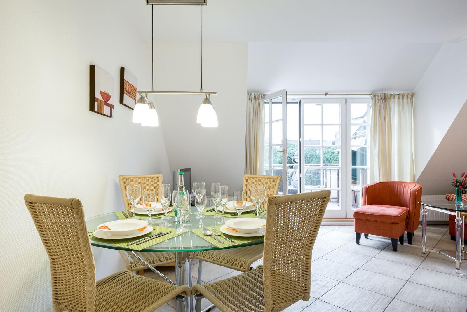 Dining table with six chairs and glass top. Background: window and armchair.