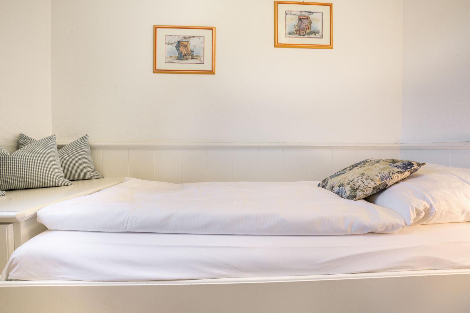 A bed with white sheets and pillows. Two framed pictures hang on the wall.