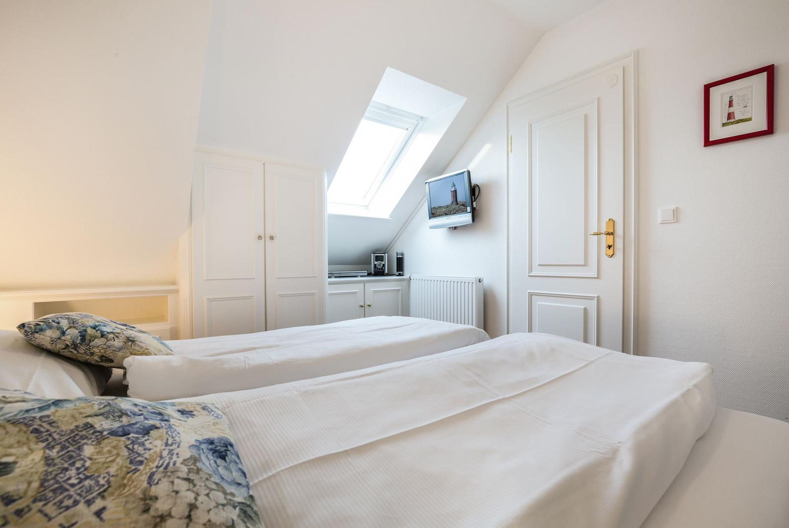 Room with two beds, sloped ceiling, skylight, and TV mounted on wall.