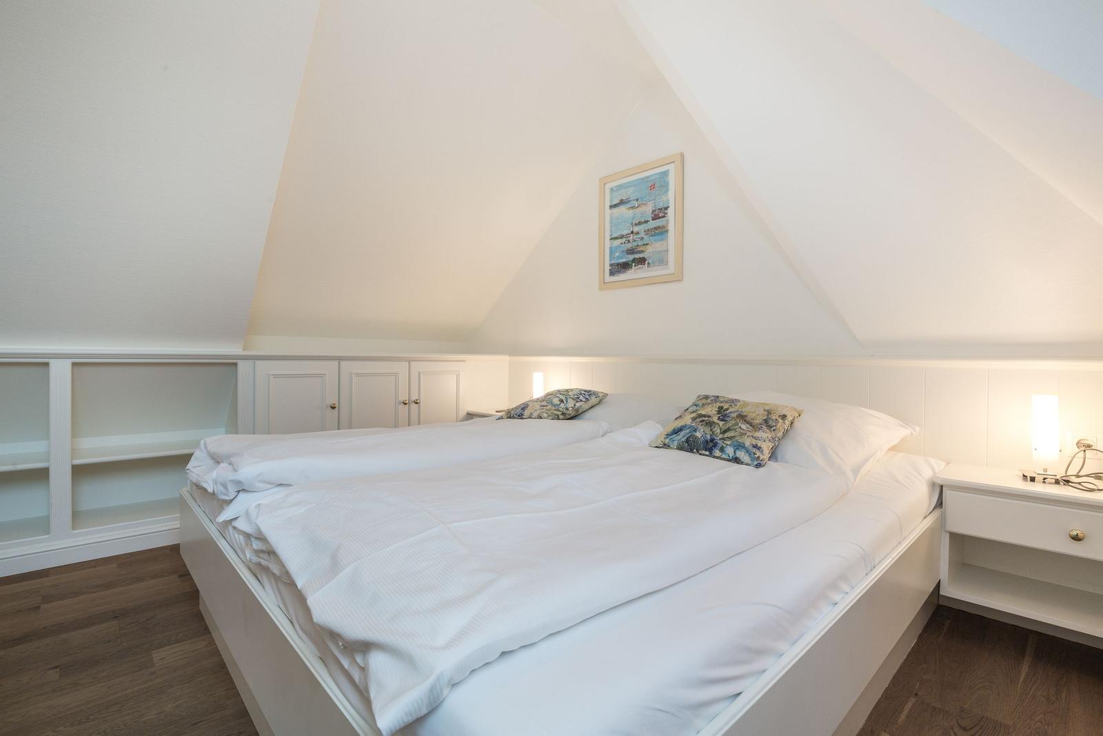 Bedroom with double bed, nightstand, and wall art under sloped ceiling.