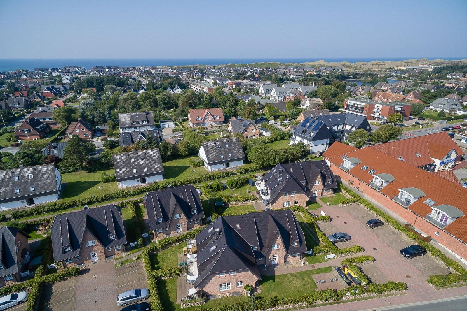 Aerial view of residential area with houses, gardens, and ocean in background.
