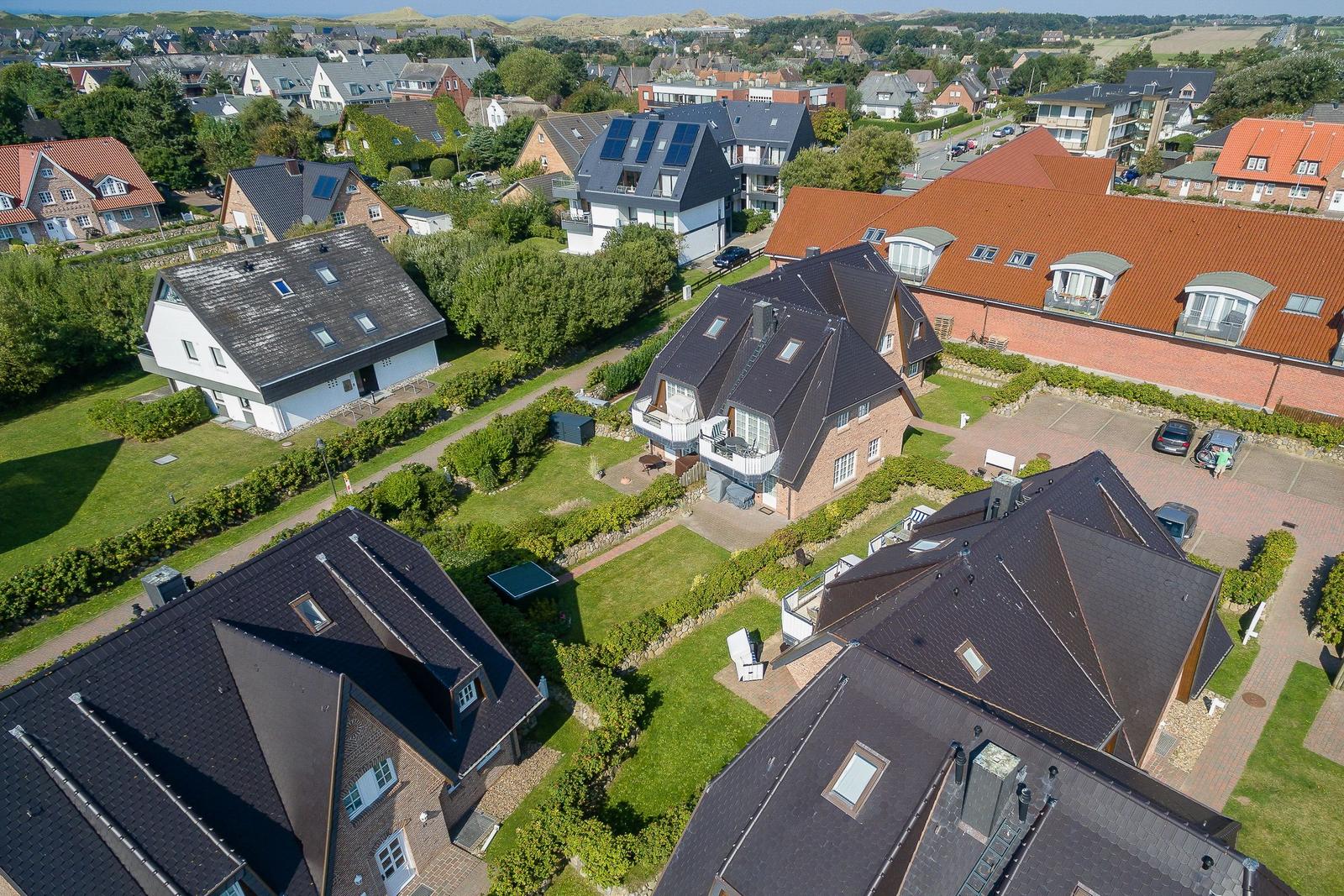 Aerial view of residential houses with gardens and roofs in a town setting.