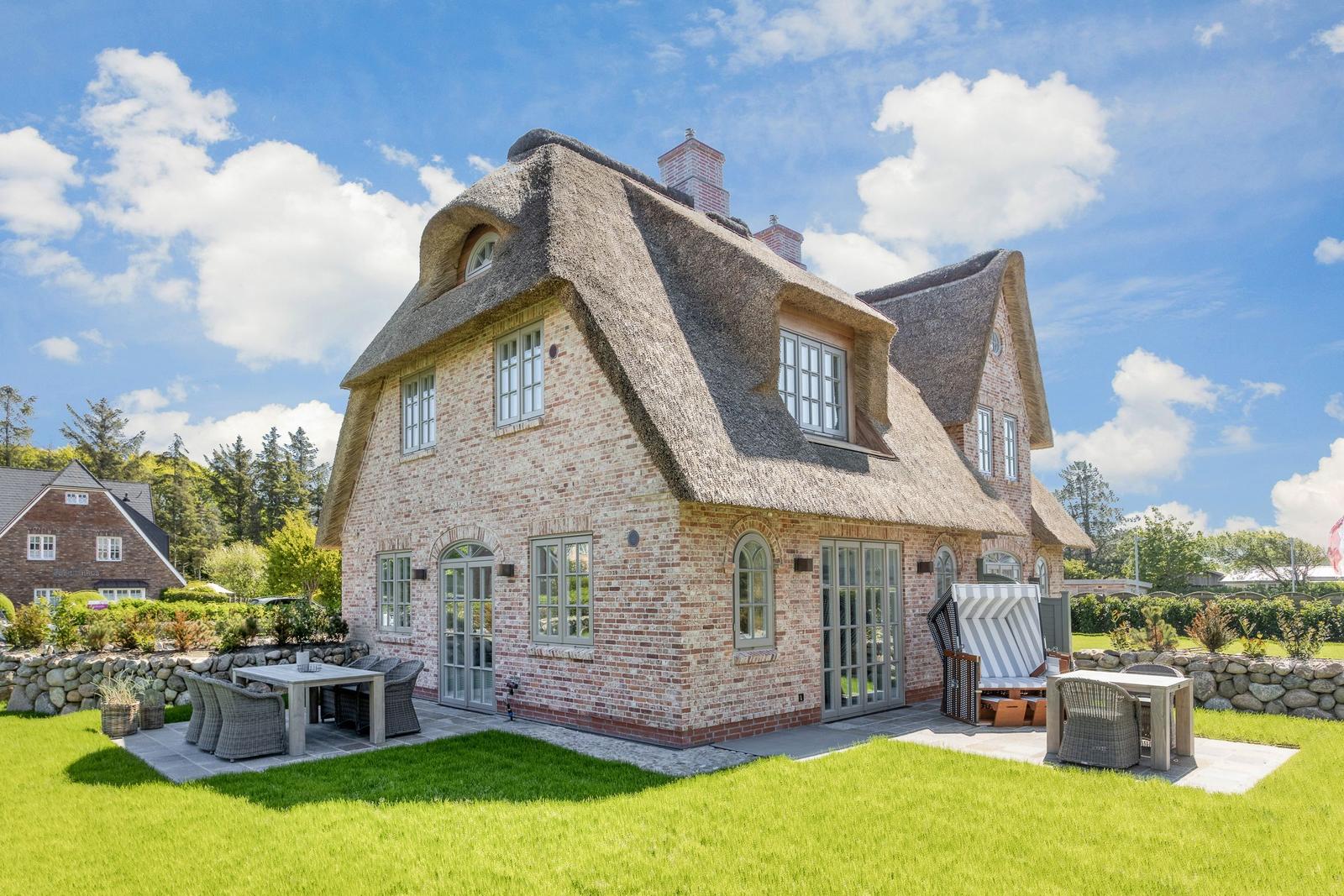 House with thatched roof, terrace, and garden. White windows and wooden doors.