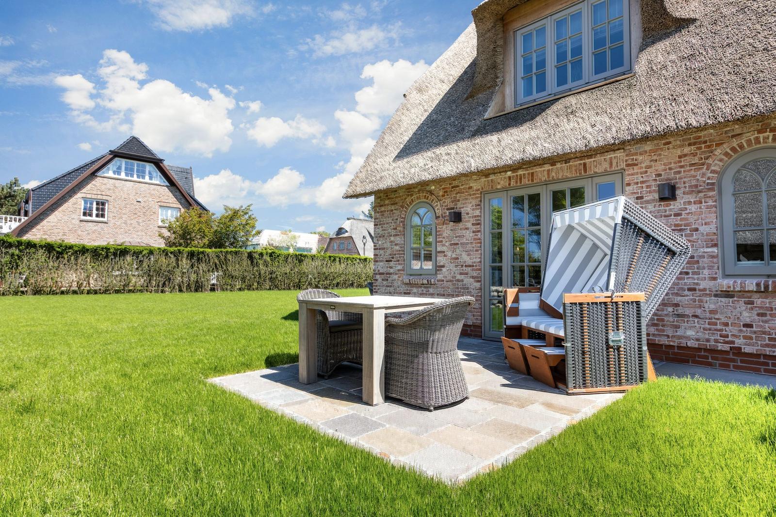 House with thatched roof, terrace, and garden. Outdoor table, chairs, and lounge chair.