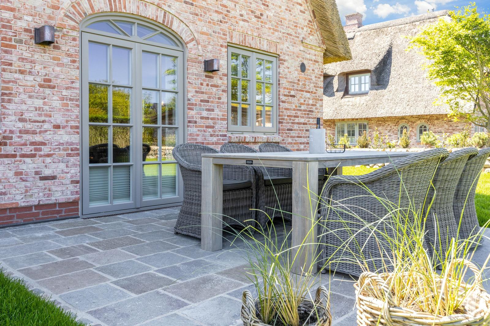 Terrace with table and chairs in front of brick house with sliding doors.