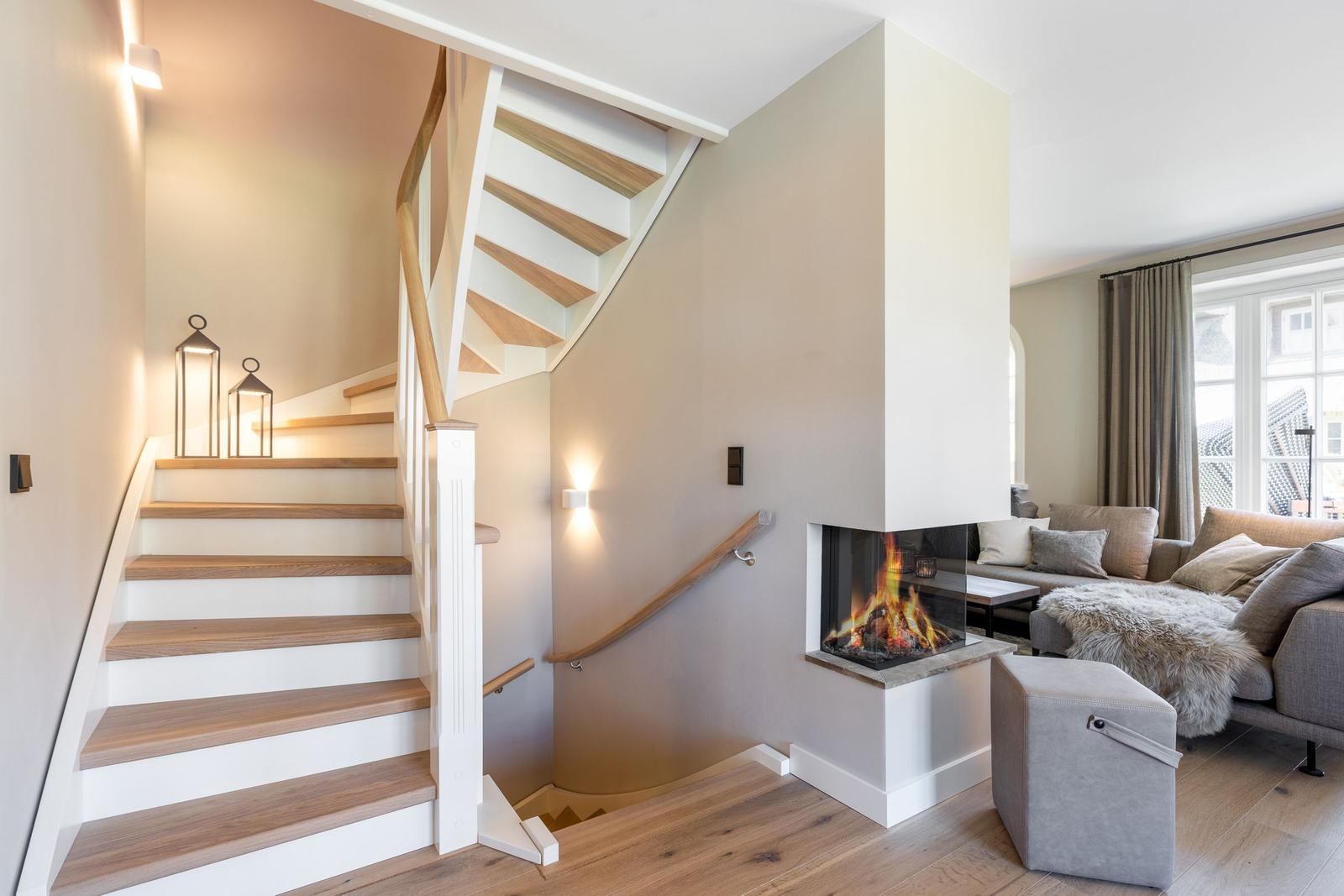 Staircase with wooden steps and handrail, fireplace, and living area with sofa and window.