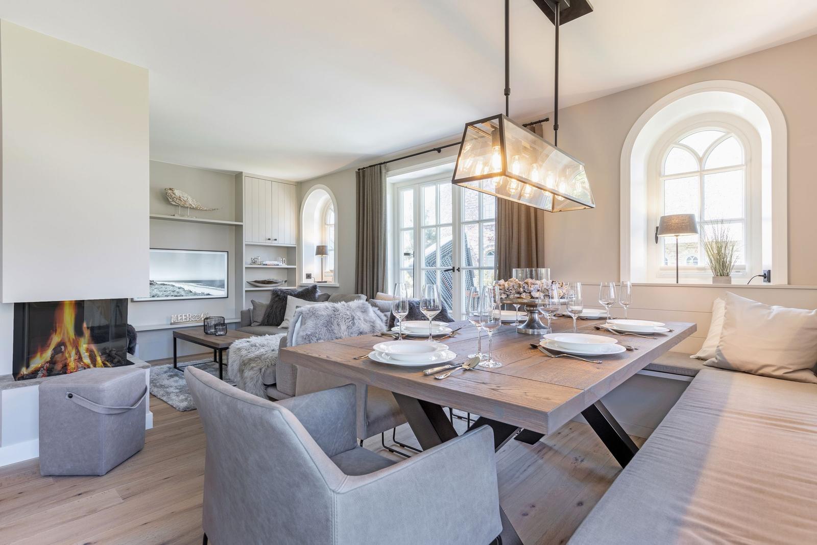 Dining area with wooden table, bench, and modern pendant light. Living area with fireplace in background.