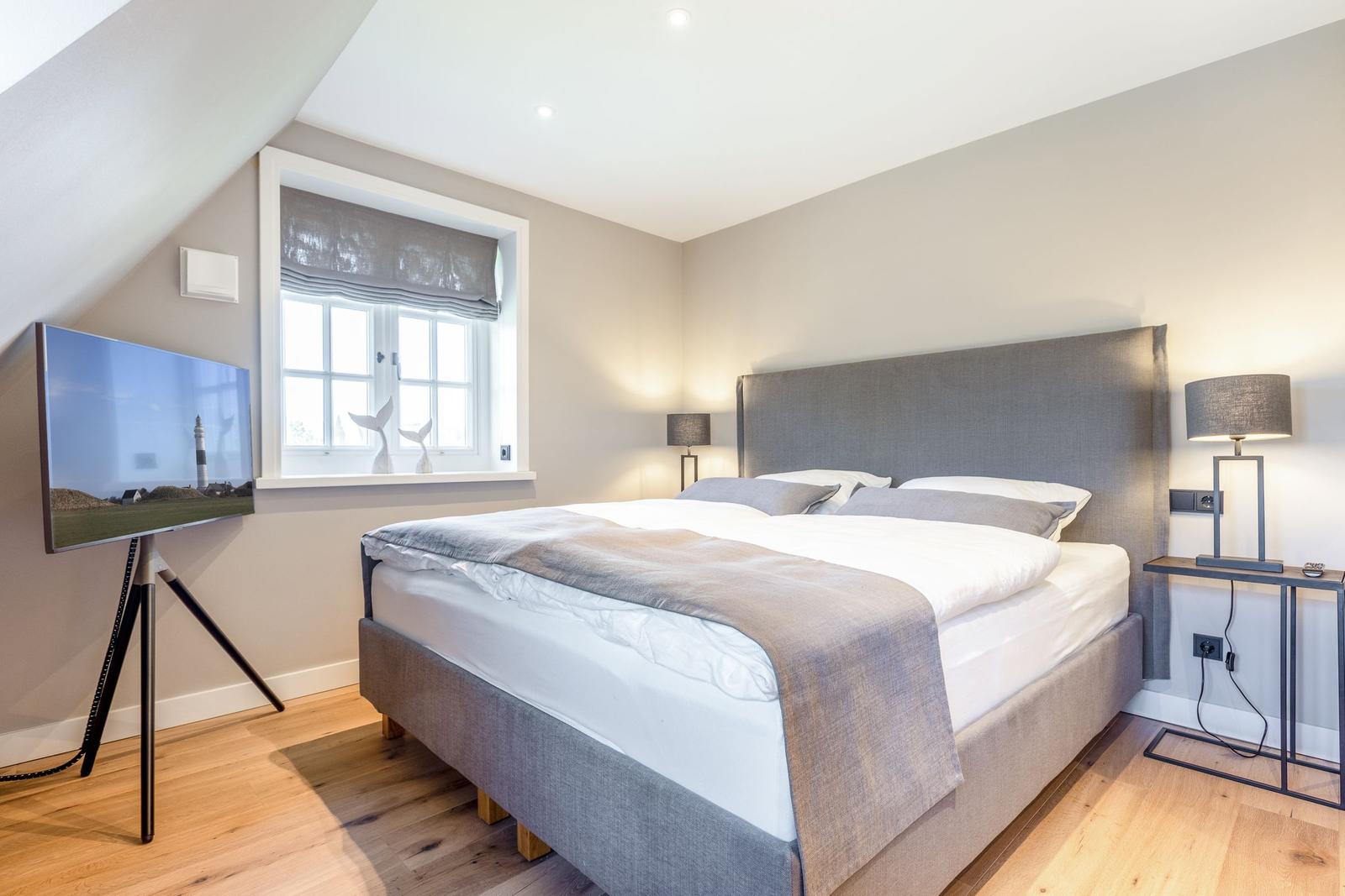 Bedroom with double bed, window, and TV on stand.